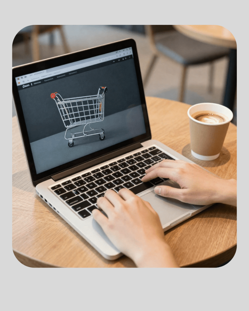 Een persoon die typt op een laptop met een website die een winkelwagentje toont, terwijl er een beker koffie op de houten tafel staat.